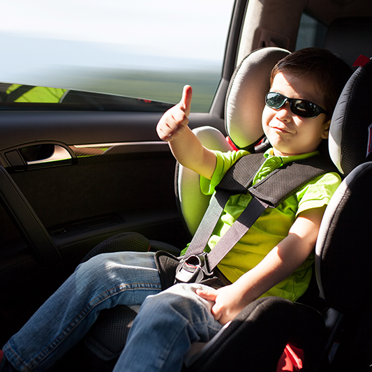 happy child giving thumbs up in a car seat